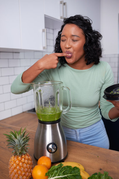 一位年轻的多民族妇女在厨房品尝她刚做的绿色奶昔图片下载