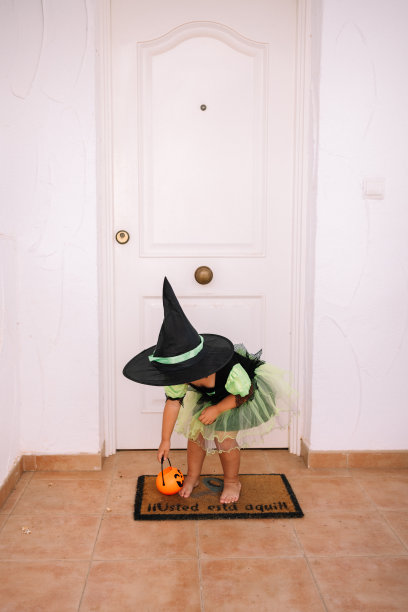 穿着女巫服装的小女孩在白色的门口玩不给糖就捣蛋的游戏图片下载