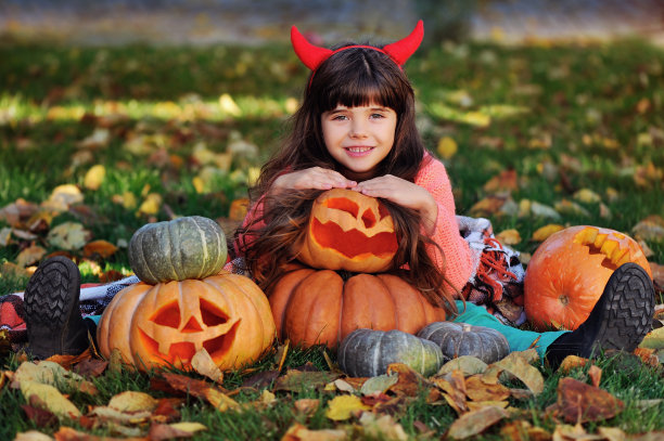 秋天的草坪上，漂亮的女孩拿着雕刻的万圣节南瓜图片下载
