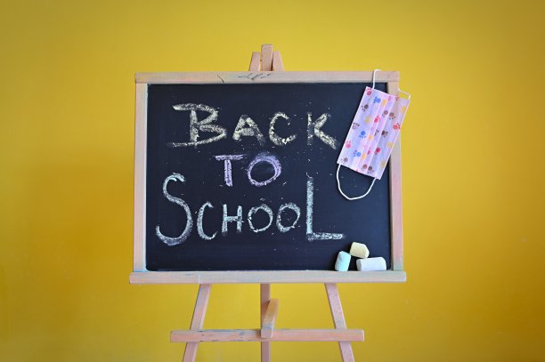 黑板——回到学校。黄色的背景是教育和学校的概念。佩戴口罩预防新冠病毒感染。图片下载