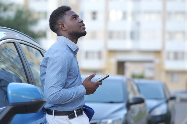 英俊的年轻商人站在他的车旁边，使用智能手机图片下载