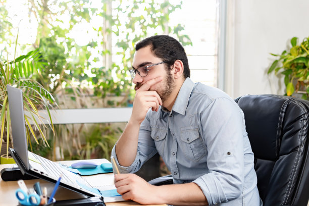 在家庭办公室使用笔记本电脑做笔记的沉思企业家图片下载
