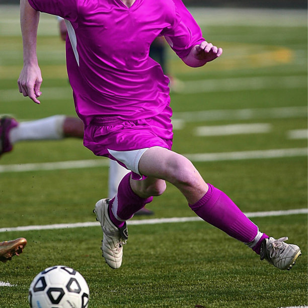身穿没有品牌的粉红紫色运动服的白人正在草地上踢足球素材图片