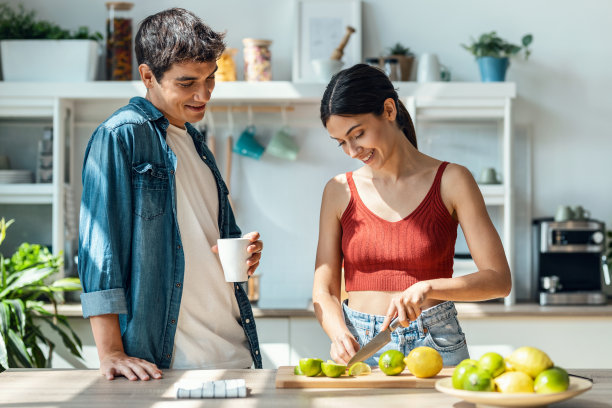 健康的年轻女子在家里的厨房里一边切新鲜的水果，一边烹饪健康的食物。图片下载