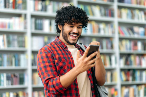 兴奋的印度人或阿拉伯人，自由职业者或学生，用他的智能手机，看着屏幕，为成功、胜利而高兴，做了yes的手势，开心地微笑。小玩意概念，无线技术图片下载