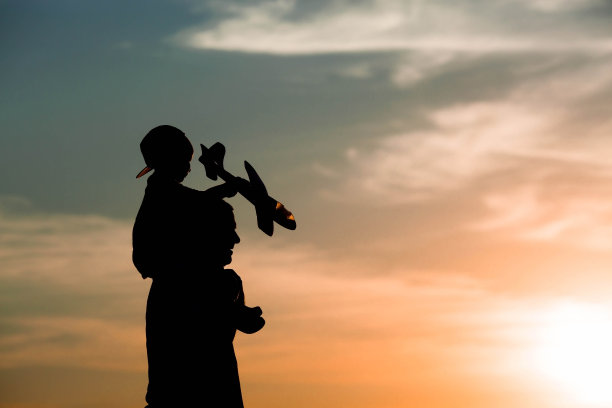 父亲和儿子在日落时发射一架玩具飞机。人们在天空映衬下的剪影。一个友好家庭的概念和父亲节。空中旅行。去旅行，坐飞机，度个假。图片下载