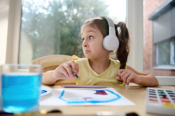 开朗的小女孩戴着耳机用画笔和水彩画画画。儿童创意艺术课程图片下载