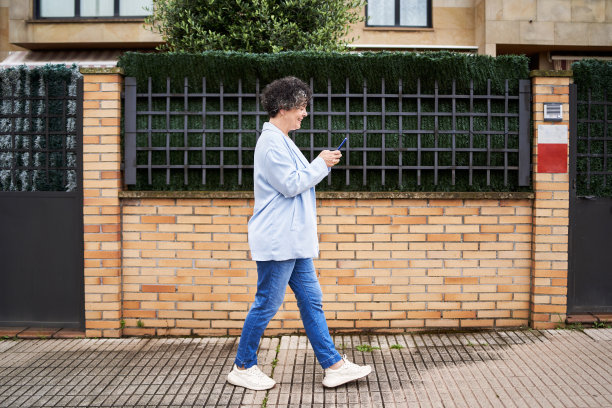 一个成熟的女人走在她家附近的人行道上，背景是一所砖墙的房子图片下载
