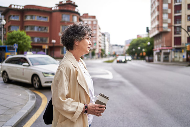 一个成熟的女人拿着可重复使用的咖啡杯，看着红绿灯过马路图片下载