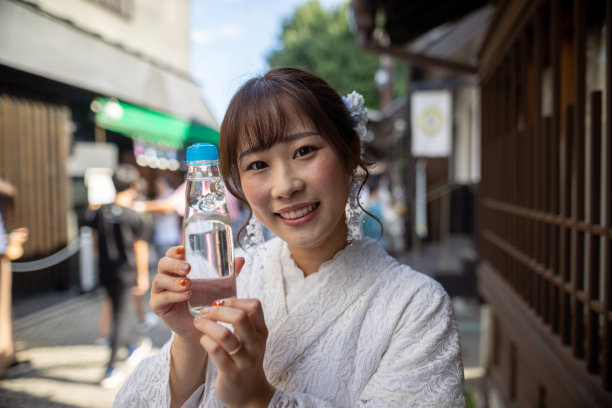身穿白色夏季和服的女子，手持“Ramune”汽水，站在日本传统购物街上图片下载