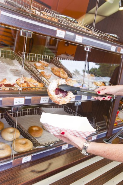 一名妇女从一家咖啡店的展示品中取出一块糕点图片下载