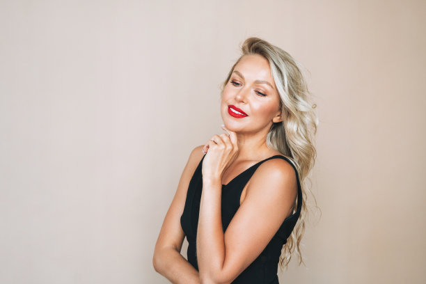 华丽美丽的金发年轻女子的肖像与明亮的化妆在晚礼服上的米色背景图片下载