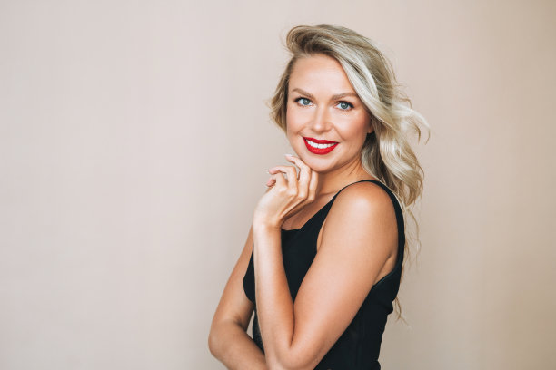华丽美丽的金发年轻女子的肖像与明亮的化妆在晚礼服上的米色背景图片下载