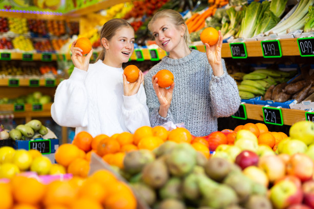快乐的少女和母亲拿着成熟的橙子在蔬菜杂货店图片下载