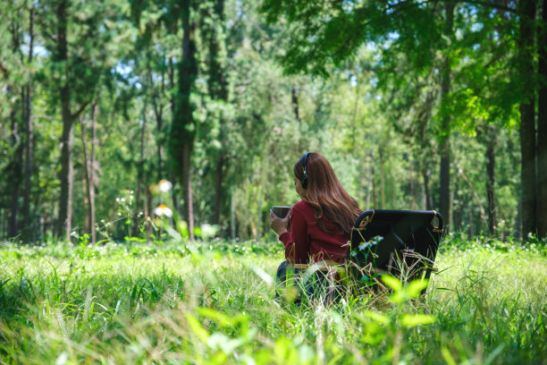 一位女士坐在公园的露营椅上，一边戴着耳机听音乐，一边喝咖啡图片下载