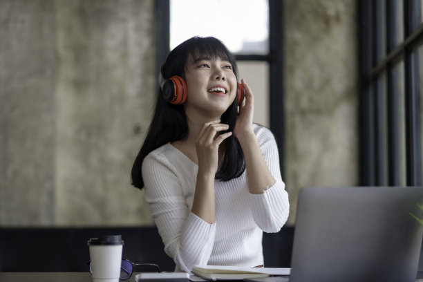 可爱的亚洲女人戴着耳机坐在家里听音乐，开心地享受着听音乐的乐趣。图片下载