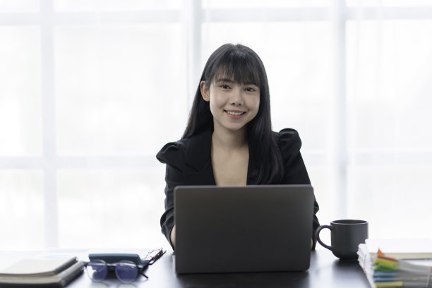 美丽的亚洲商务女性正在用笔记本电脑在办公室工作，脸上带着愉快的表情。图片下载