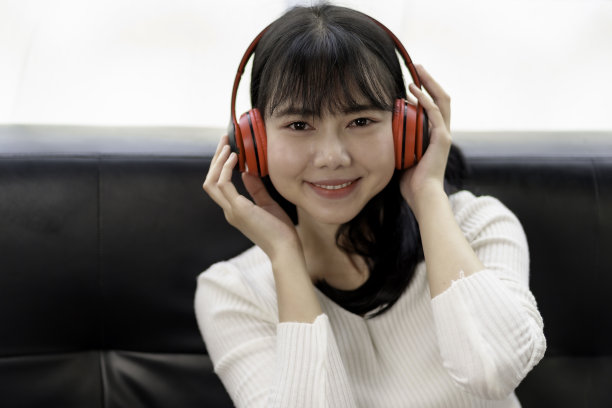 可爱的亚洲女人戴着耳机坐在家里听音乐，开心地享受着听音乐的乐趣。图片下载