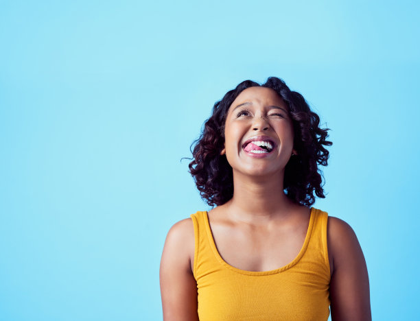 快乐的黑人女性，一张滑稽的脸，吐着舌头在牙齿上，蓝色的背景。有趣的疯狂女孩，为美丽和女性独立而兴奋。用微笑庆祝生命图片下载