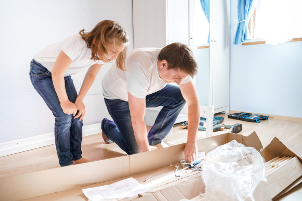 爸爸，小女孩女儿按照指示在儿童房组装木制婴儿床。帮助父亲，安装孩子们的家具。自组装的指南。家人一起活动。家居设计图片下载