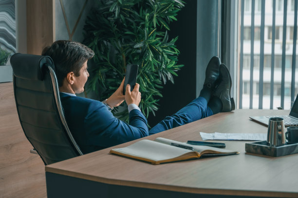 西装革履的商人，手里拿着手机。男人输入信息，使用社交网络。检查消息。商务会议。现代办公室。总经理、首席执行官。打电话来的合作伙伴。计划工作时间图片下载