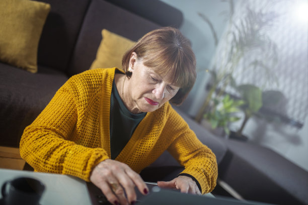 一个严肃的女人穿着黄色毛衣在家工作的照片。图片下载
