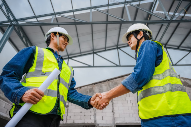 土木工程师拿着图纸，在改造现场与建筑师握手。土木工程师在建筑工地检查建筑物。图片下载