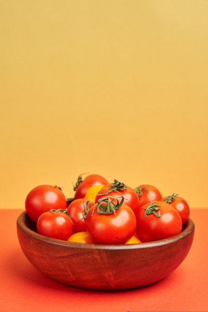 诱人的红色和黄色西红柿在明亮的橙色和红色背景下放在一个木碗里图片下载