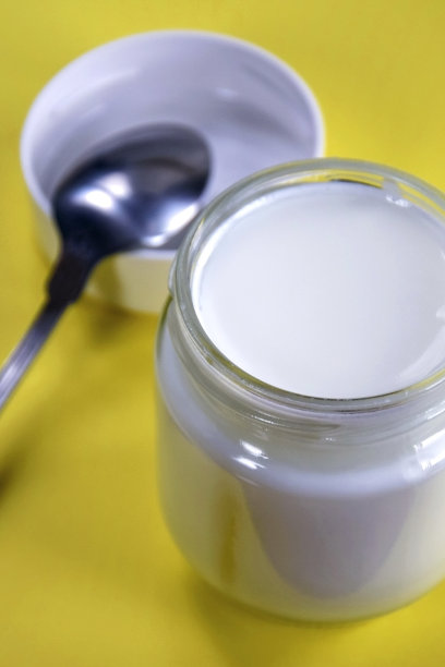 一份新鲜的天然自制有机酸奶放在玻璃罐里，勺子放在黄色的背景上。特写镜头。图片下载