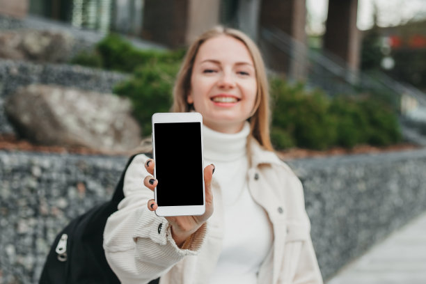 快乐微笑的女学生在大学背景下展示手机。模型设计图片下载