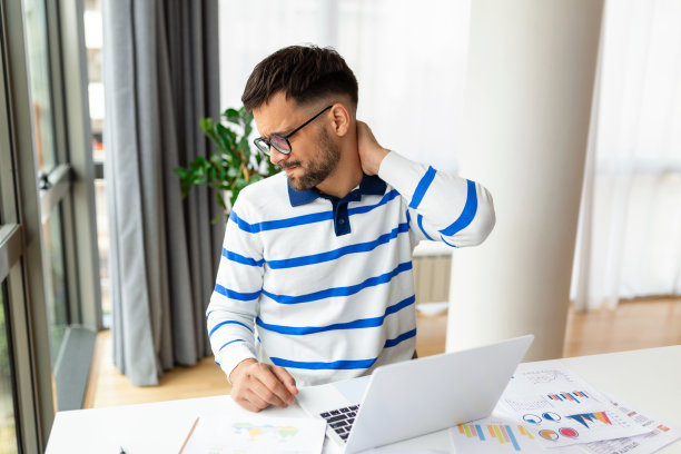 商人拿着笔记本电脑坐在桌子前后感到脖子疼。因长时间在电脑上工作而患上办公室综合症的疲劳男子。他正在按摩他紧张的颈部肌肉图片下载