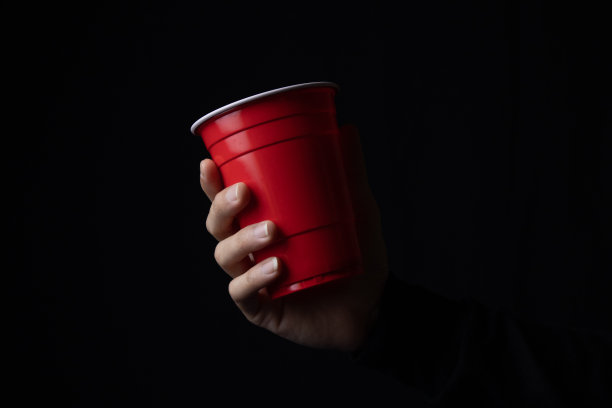红色塑料杯在黑暗中伸出一只手，特写。图片下载