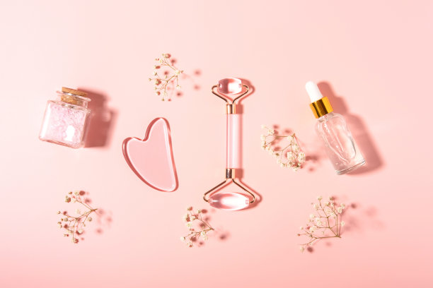 粉色石英石滚筒面部按摩水粉粉彩粉底与玻璃化妆瓶和白花。家庭水疗护理理念，美丽青春，抗衰老。前视图。平的。图片下载