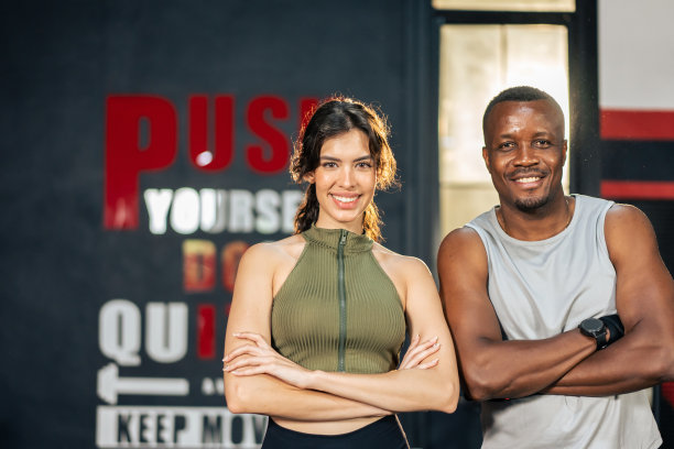 运动员在运动服装交叉手臂在健身房的肖像。拉丁裔女运动员和美国非洲裔运动员站着看相机后使用机器锻炼健康保健在健身。图片下载