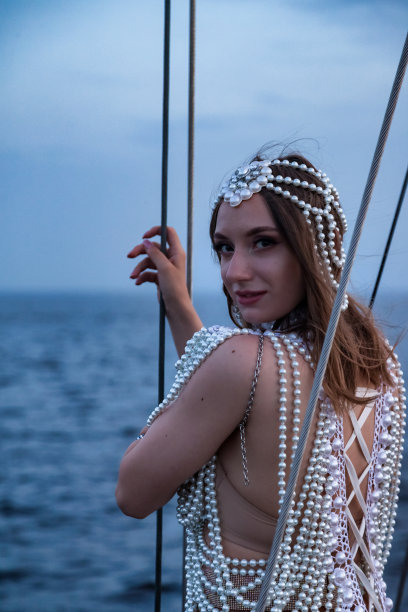 肖像女演员在白色的舞台服装在海上和蓝天背景的游艇上摆姿势，看着相机。户外穿着戏服的女性。剧场表演和趣味表演的概念图片下载