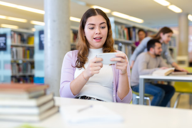 一个女学生在图书馆用手机发短信图片下载