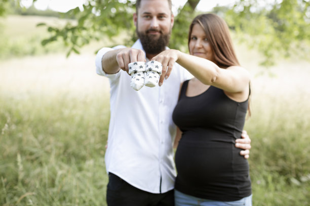 一名孕妇站在草地上，她的男友抱着婴儿袜子对着镜头图片下载