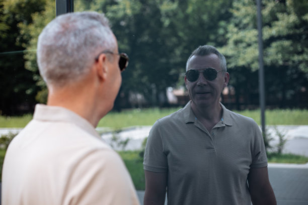 夏天，老人站在公园外，望着建筑的玻璃墙，享受着倒影的背影。图片下载