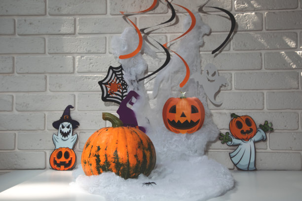 南瓜，白色的桌子上有蜘蛛网和蜘蛛，背景是白色的砖墙。万圣节构图有阴影，选择性对焦图片下载