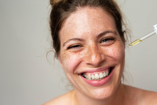 一个长着雀斑的漂亮女人用吸管往脸上涂血清图片下载