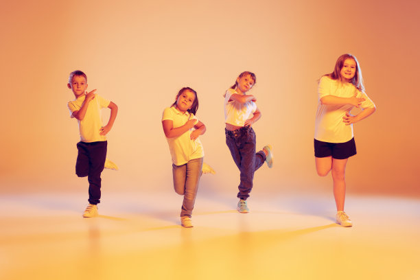一群穿着休闲服装的孩子在舞蹈课上跳舞，在霓虹灯滤光下的黄色背景下。艺术、音乐、时尚图片下载