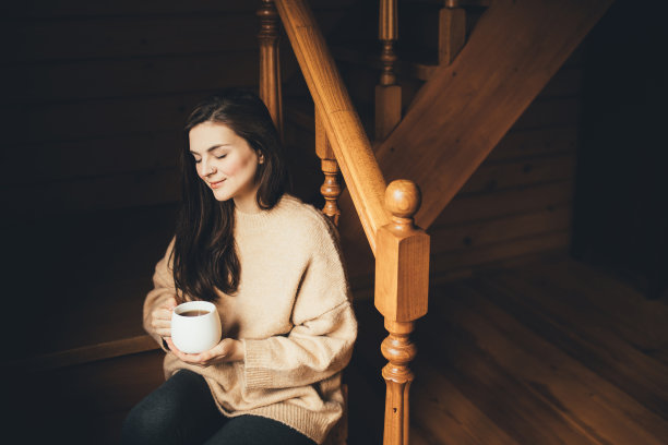 年轻女子穿着温暖的毛衣喝热茶在一个舒适的木制乡村房子。图片下载