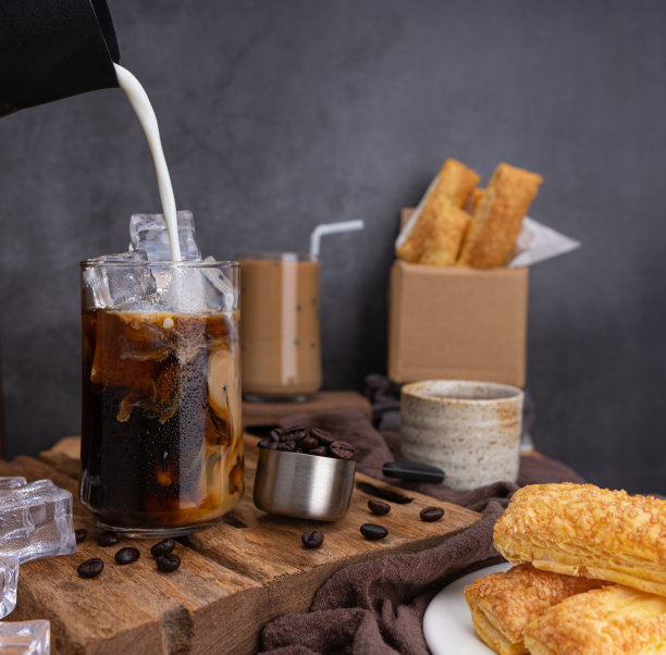 加入牛奶制作冰拿铁咖啡，夏天的咖啡在透明的玻璃，烤咖啡豆，脆皮派在木头上。黑色背景工作室照片，复制空间为您的文本图片下载