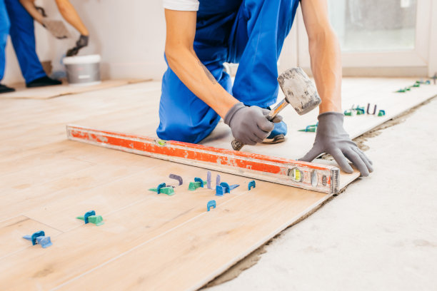 戴着灰色手套，穿着特制制服的修理工的双手敲打瓷砖，使其充分粘合图片下载