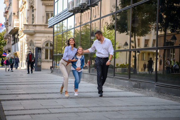 年轻的父亲和母亲牵着女儿的手走在城市的街道上。图片下载