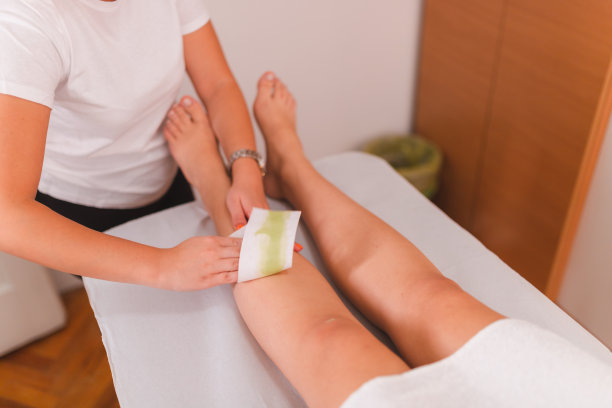 特写的美容师在一个专业的沙龙用蜡条给年轻女人的腿打蜡图片下载