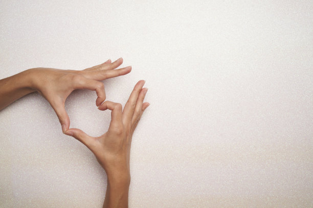 在明亮的白色背景的图片角落里，女人的手做了一个心形的手势图片下载