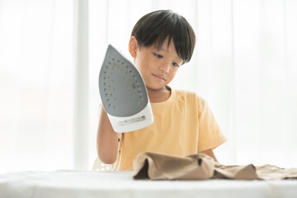 快乐小男孩周末在家用铁板熨烫校服进行房屋清洁家庭活动图片下载