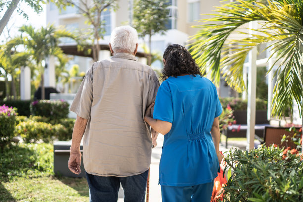 一名老年男子在女护士的帮助下到户外散步图片下载