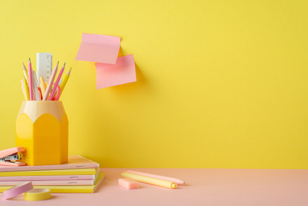 学习用品的概念。照片铅笔架堆叠的笔记本笔，胶带，迷你订书机，橡皮和便签纸贴在黄色的墙壁上的copyspace图片下载